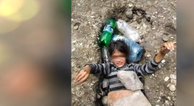 Снимка на ромско дете в дупка, затрупано с камъни и